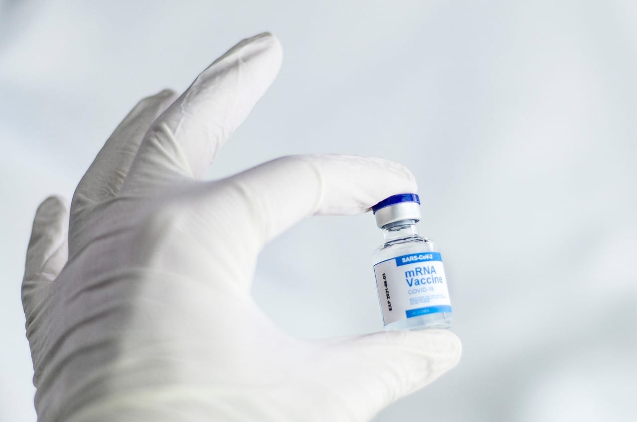 A picture of a person in white gloves holding a SARS-CoV2 mRNA Vaccine vial
